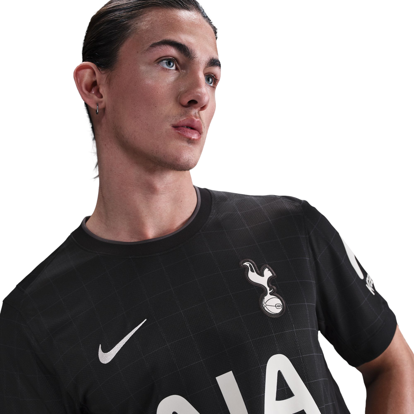 A man with slicked-back hair and blue eyes wears a black Tottenham Hotspur jersey featuring a Nike swoosh and a white crest, posed against a solid black background.