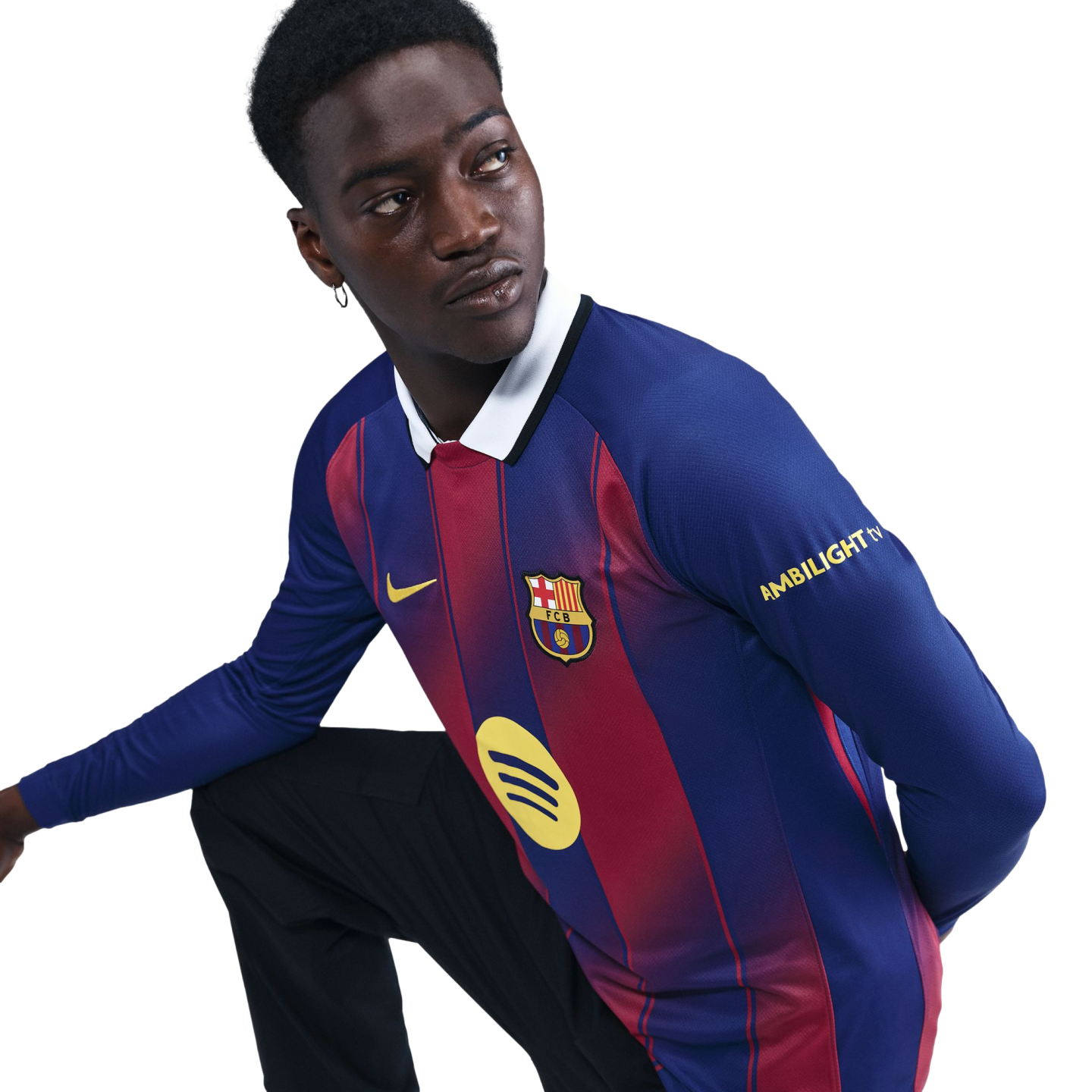 A young Black man wearing a long-sleeved FC Barcelona jersey and black pants, kneeling against a black background.