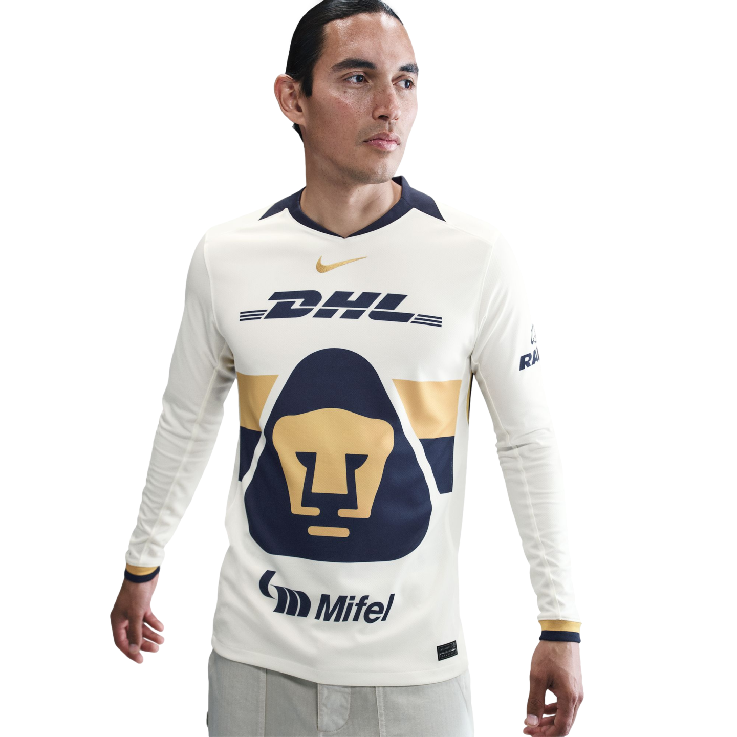 A man in a long-sleeved Pumas UNAM soccer jersey. The cream jersey features a large navy and gold feline head logo, with DHL, Nike, and Mifel branding.