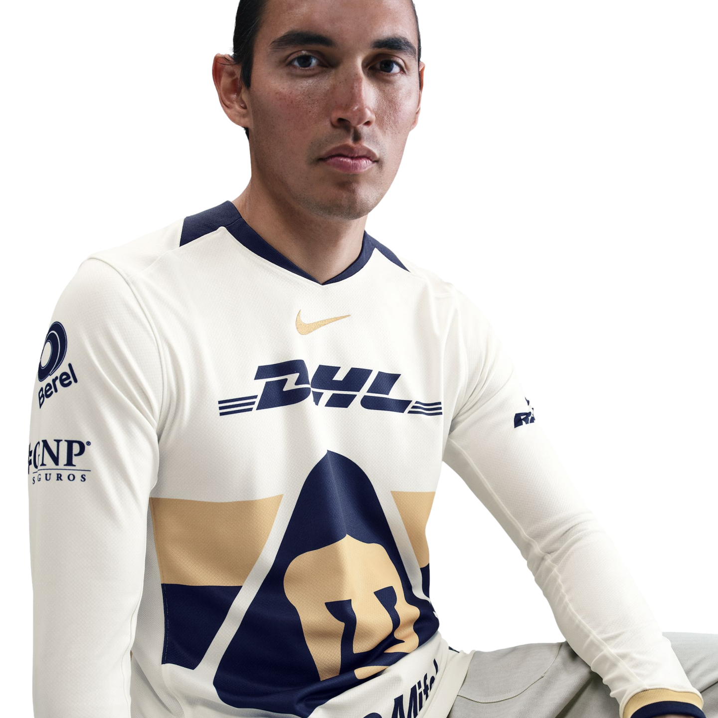A man in a cream-colored long-sleeve Pumas UNAM soccer jersey with navy and gold accents, featuring DHL and Nike logos, against a white background.