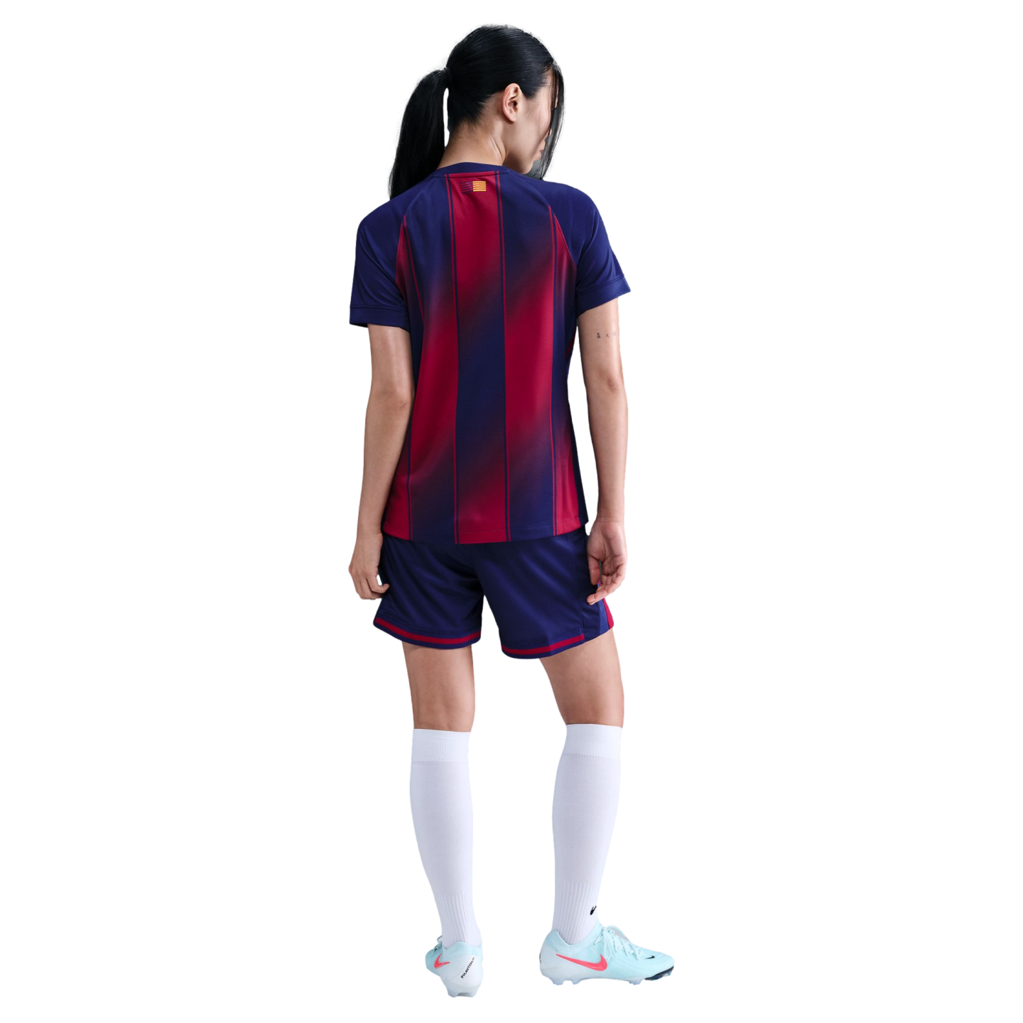 Rear view of a woman in a red and blue striped soccer kit, white socks, and light blue cleats against a black background.