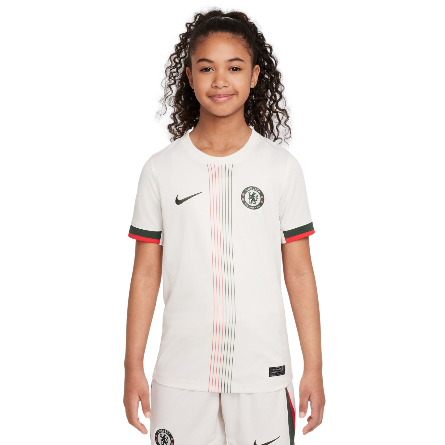 A young girl with curly hair posing in a white Chelsea FC soccer jersey with red and green accents and matching shorts.