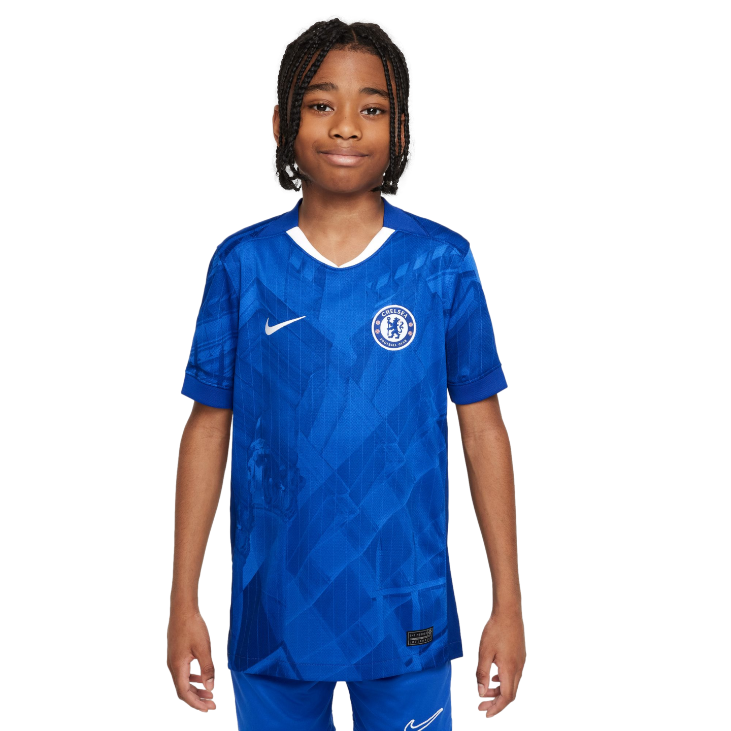 A young boy with braided hair smiling while wearing a blue Nike Chelsea FC football jersey against a plain white background.
