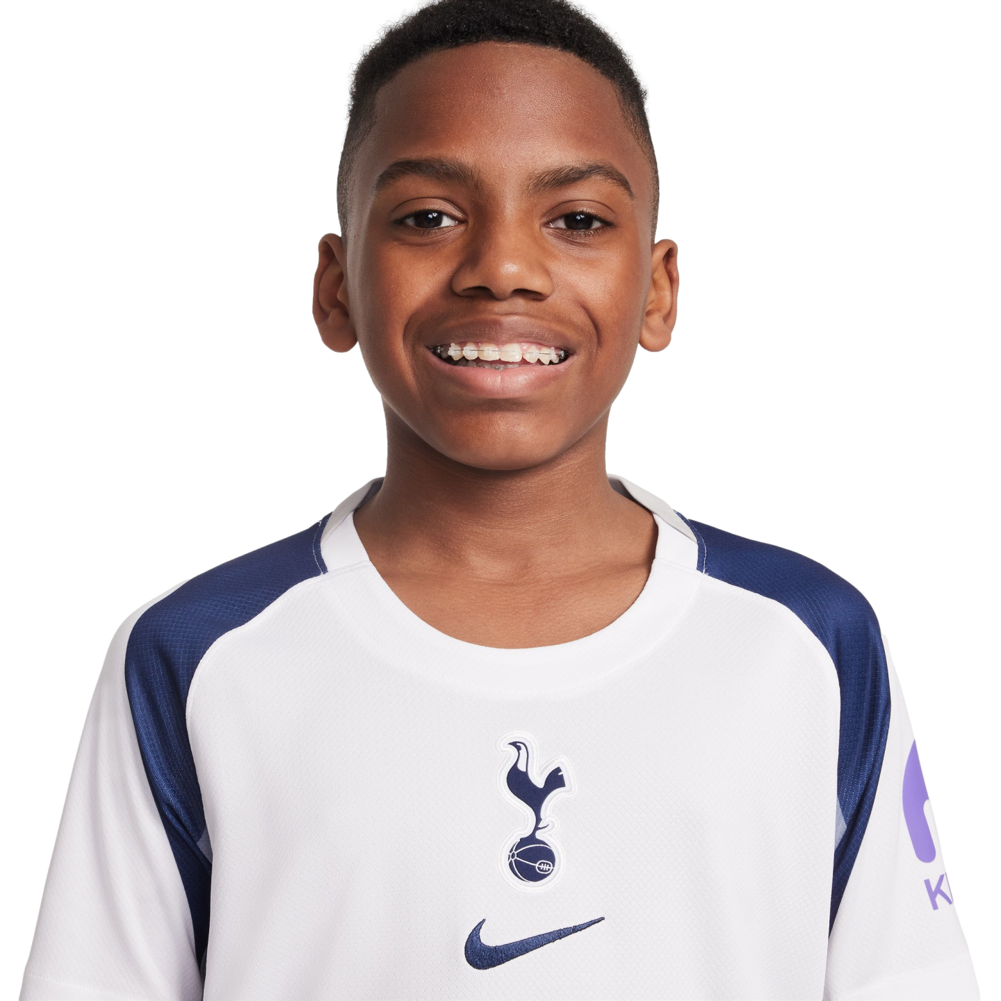 Portrait of a smiling young Black boy with braces, wearing a white and navy blue Tottenham Hotspur football jersey against a plain white background.