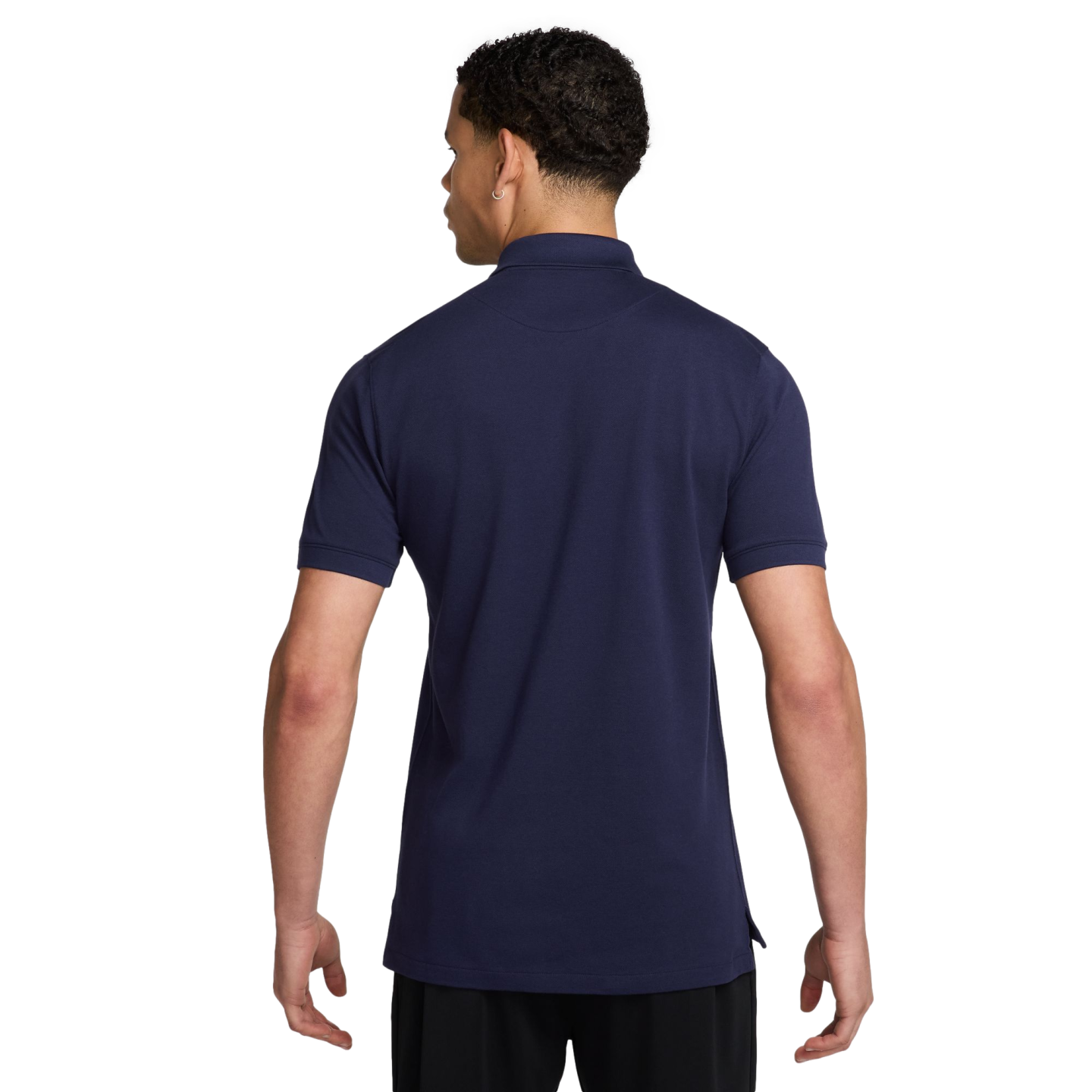 Rear view of a man wearing a navy blue short-sleeve polo shirt and black shorts against a solid black background.