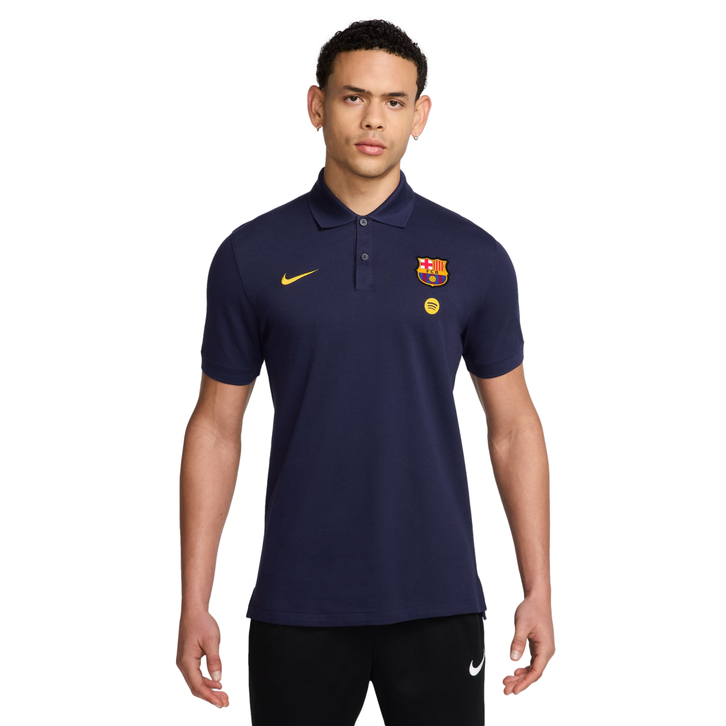 A man wearing a navy blue Nike FC Barcelona polo shirt with yellow branding and black Nike joggers, against a solid black background.