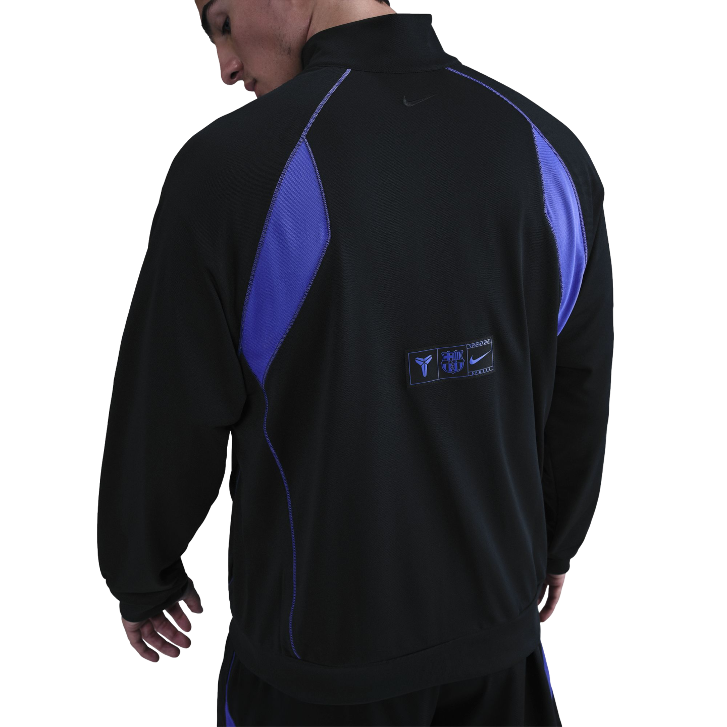 Rear view of a man wearing a black and purple sports jacket with FC Barcelona and Kobe Bryant logos on the lower back.