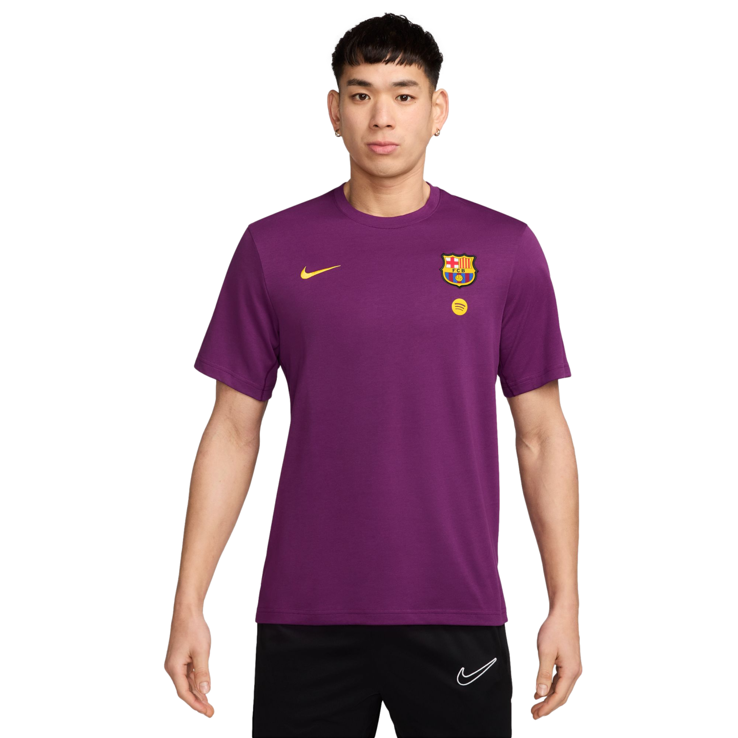 A young man models a purple short-sleeve FC Barcelona t-shirt with gold Nike and Spotify logos, and club crest, paired with black Nike shorts.