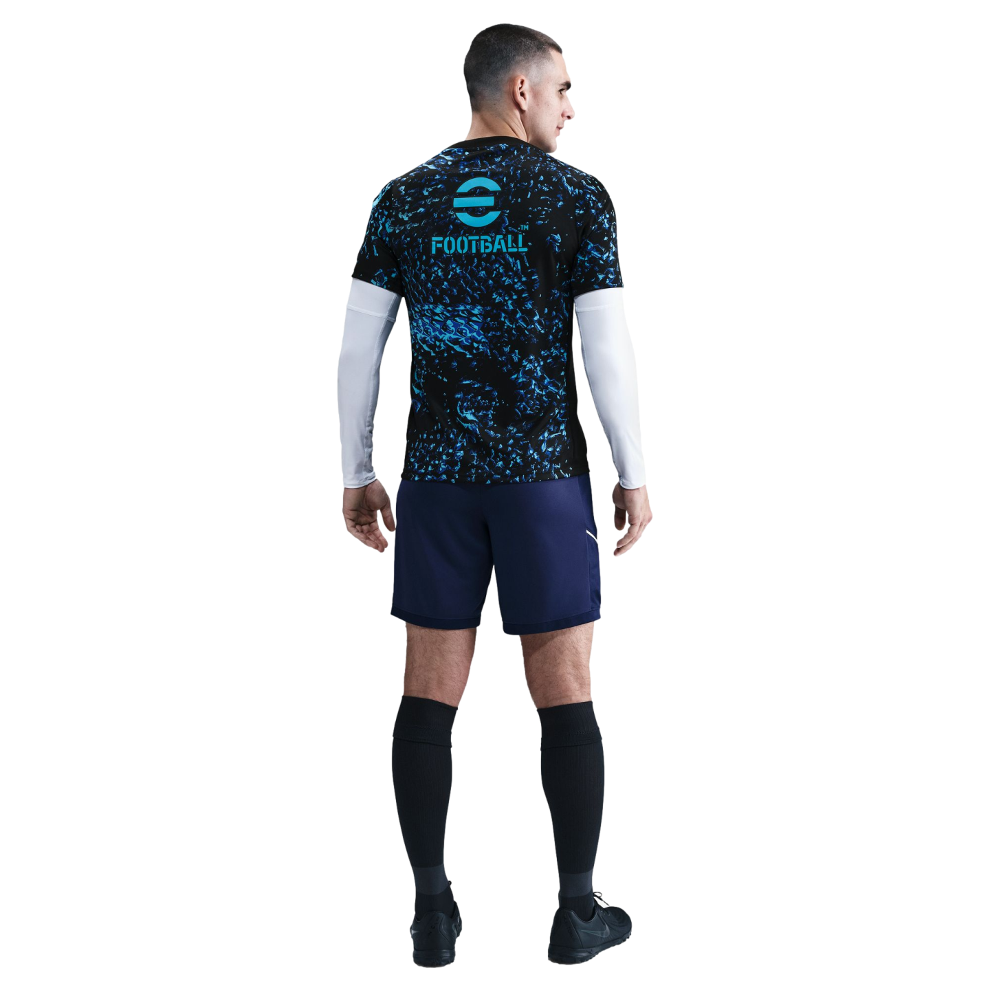 Back view of a man in a black and blue patterned football jersey, navy shorts, and black socks against a white background.