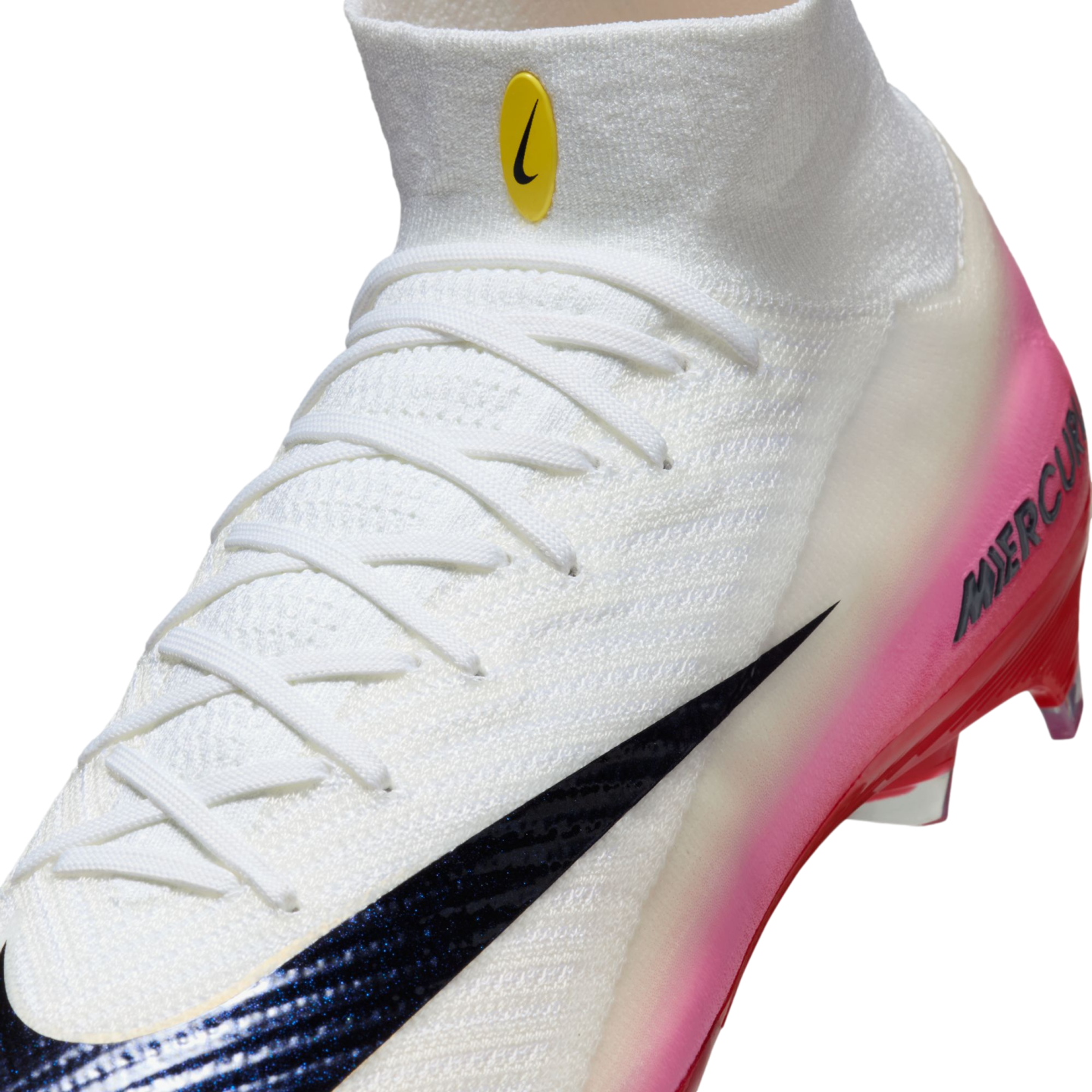 Close-up of a white Nike Mercurial soccer cleat with white laces, a black swoosh, and a pink gradient heel. A small yellow logo is on the white knit ankle collar.