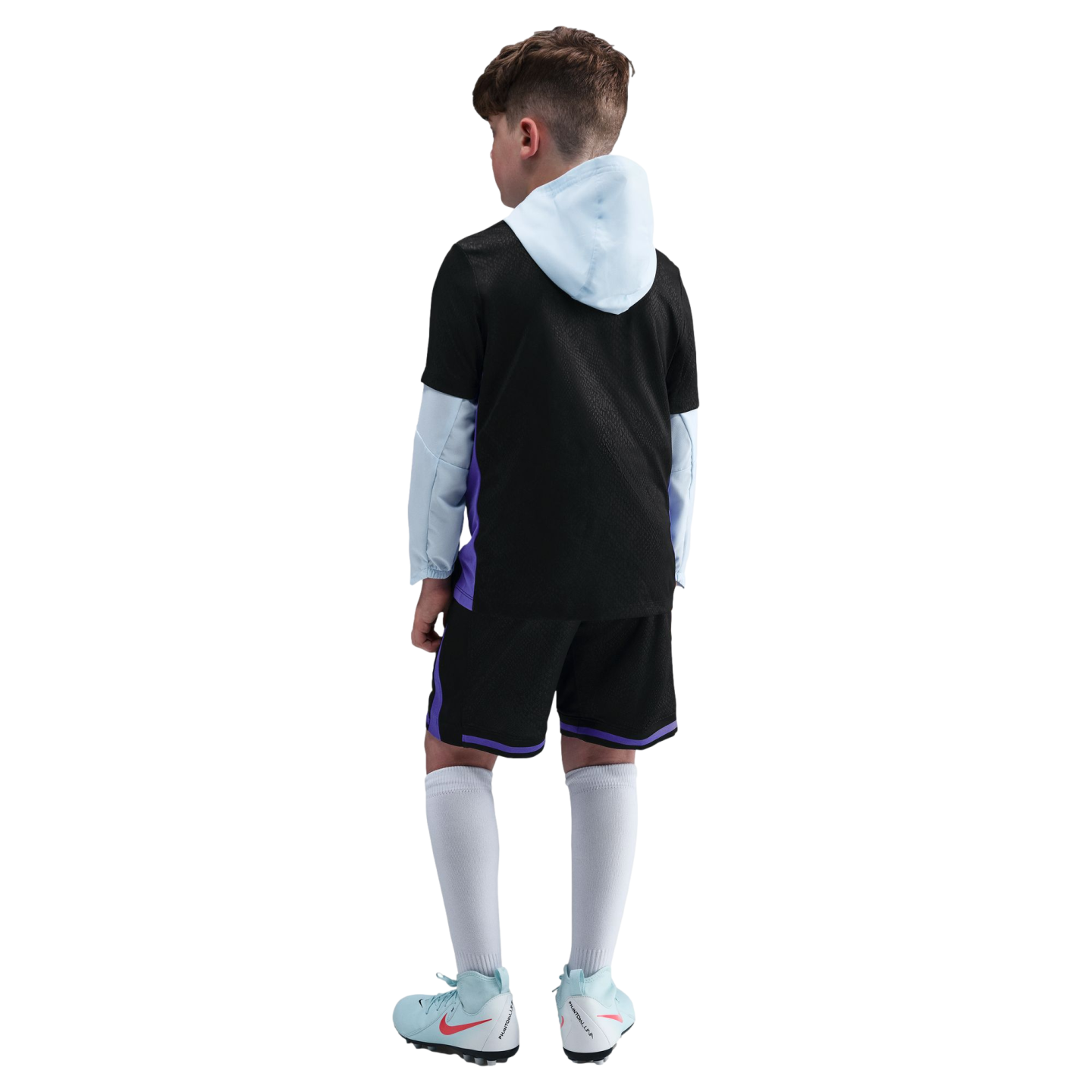Back view of a boy wearing a black and light blue hooded soccer uniform and cleats, standing against a solid black background.