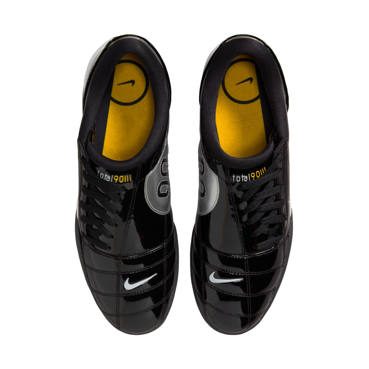 Top-down view of shiny black Nike Total 90 III soccer shoes with yellow insoles and small white swooshes on the toes, against a white background.