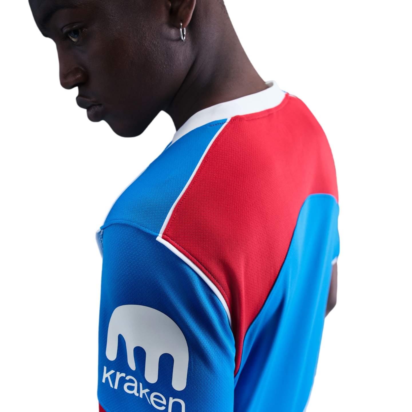 A person wearing a blue and red athletic jersey with a white 'Kraken' logo on the sleeve, looking down against a black background.
