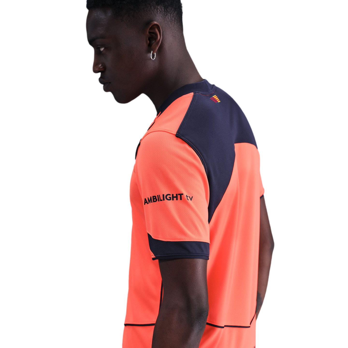 Profile of a man wearing a bright orange and navy blue athletic shirt with "AMBILIGHT tv" on the sleeve, set against a solid black background.