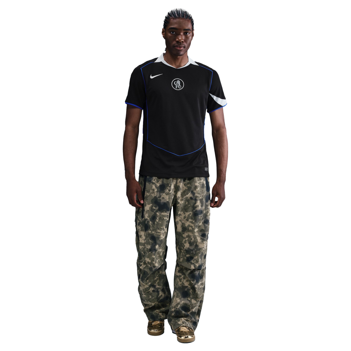 Man wearing a black Nike Chelsea FC jersey, camouflage cargo pants, and gold metallic sneakers against a black background.