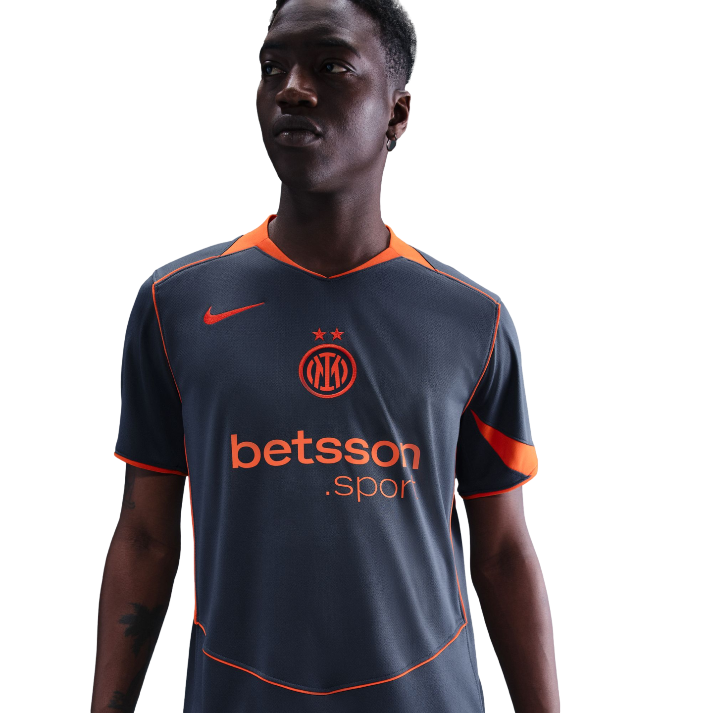 A man wearing a grey and orange Nike Inter Milan soccer jersey with a Betsson.sport logo, looking to the side against a black background.