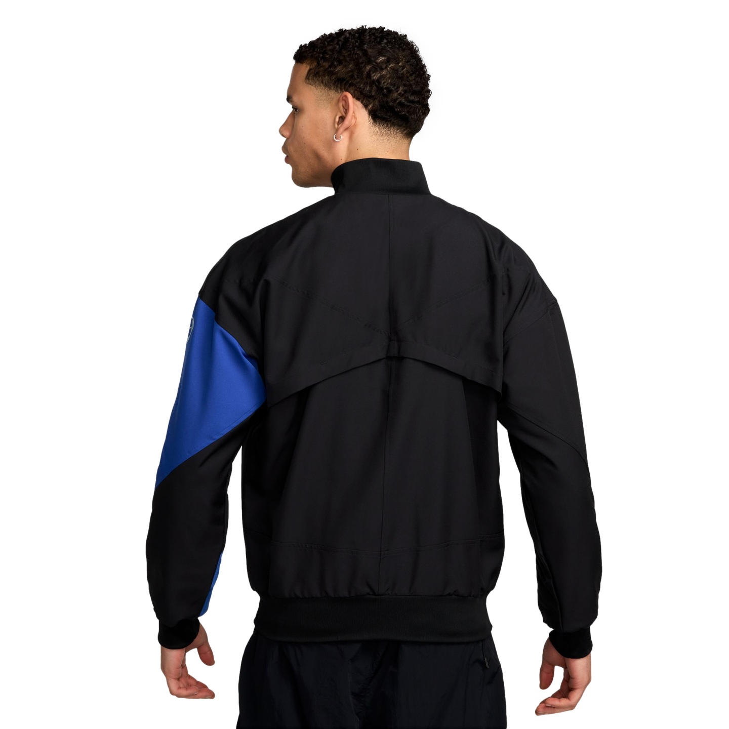 Rear view of a person wearing a black jacket with a blue sleeve panel and matching black pants, set against a solid black background.