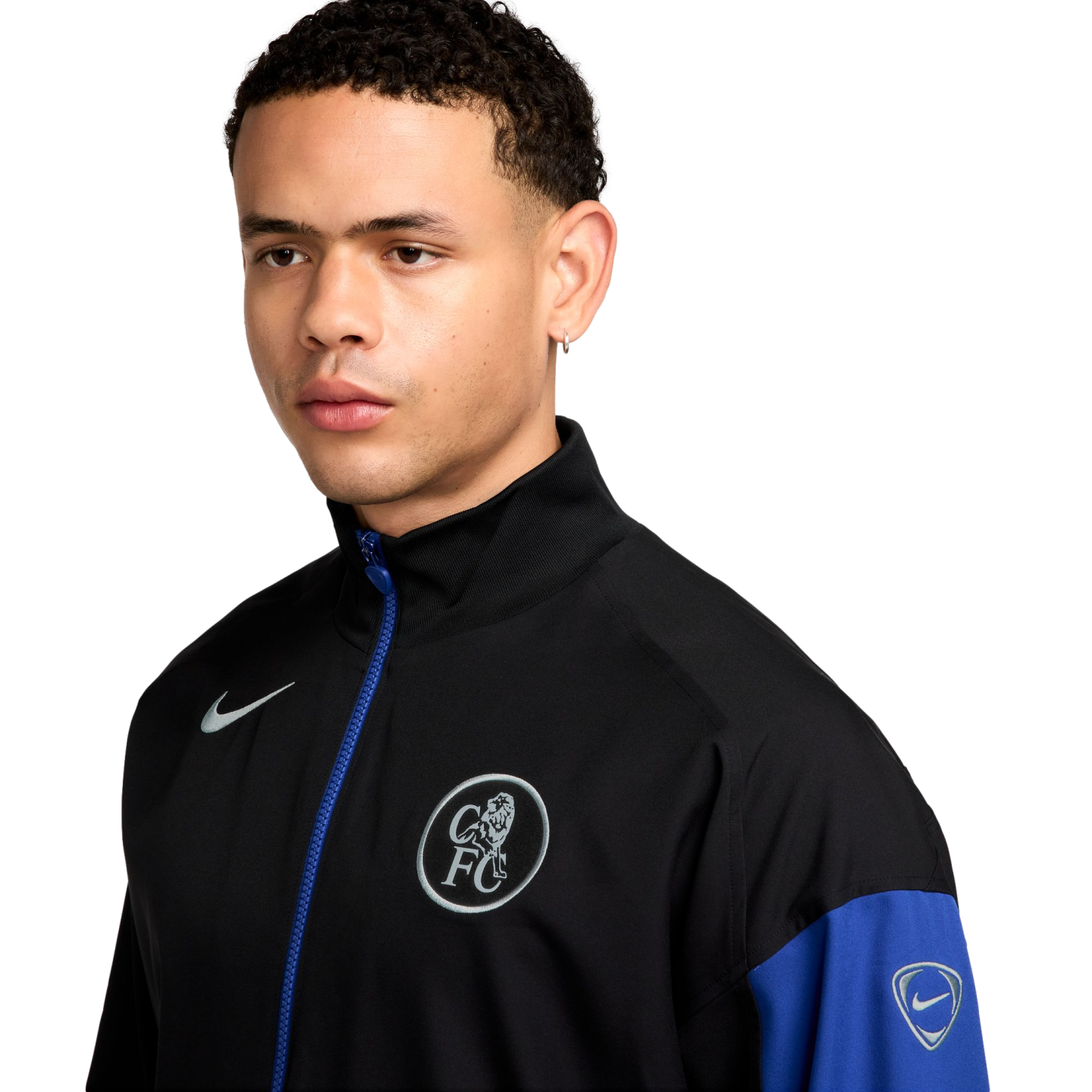 A man wearing a black and blue Nike Chelsea FC track jacket against a black background.