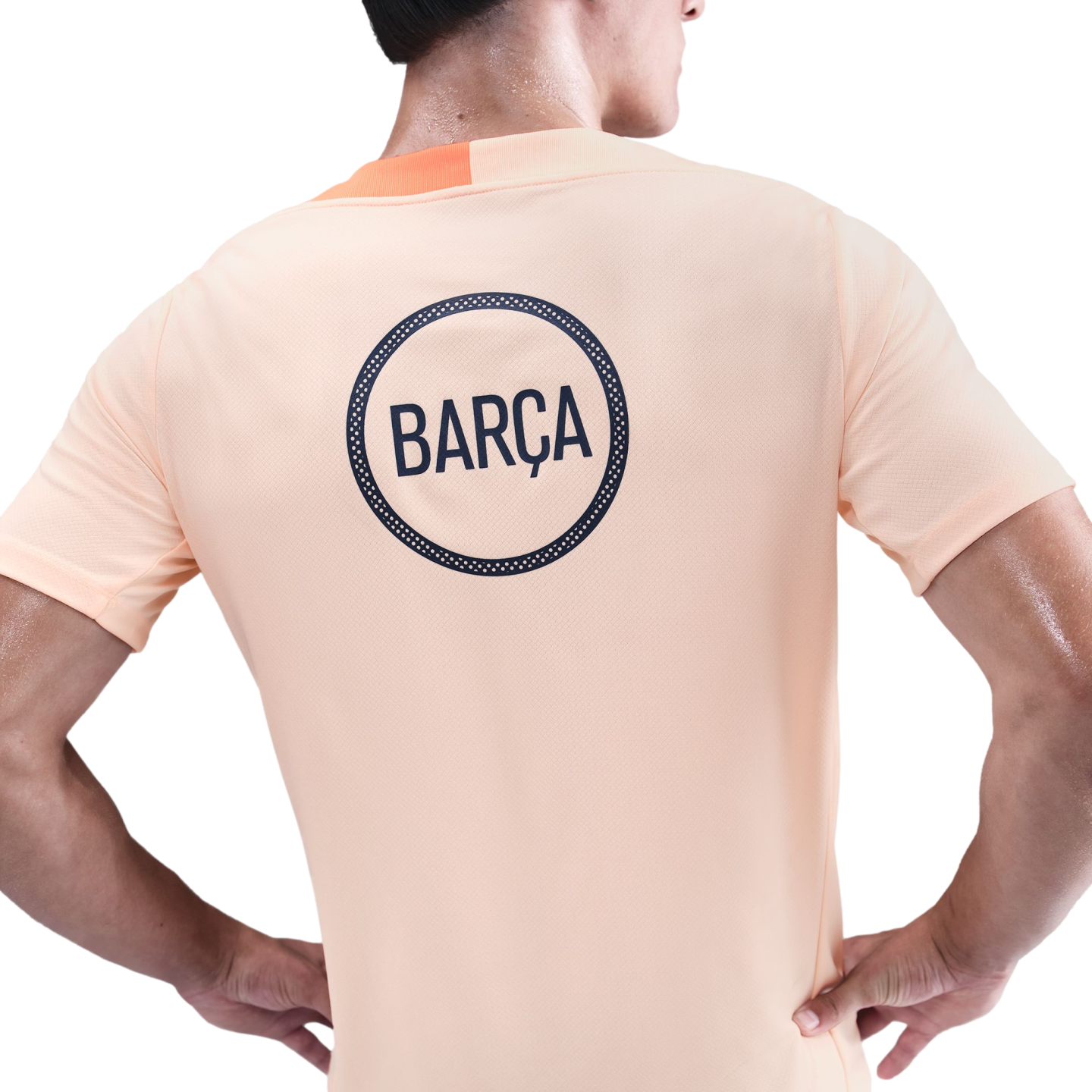 Back view of a person wearing a light orange t-shirt with a navy blue circular logo reading "BARÇA" on the back.