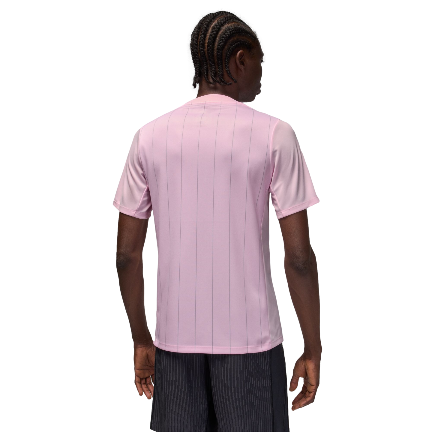 Rear view of a person with braided hair wearing a light pink pinstriped t-shirt and dark pinstriped shorts against a solid black background.