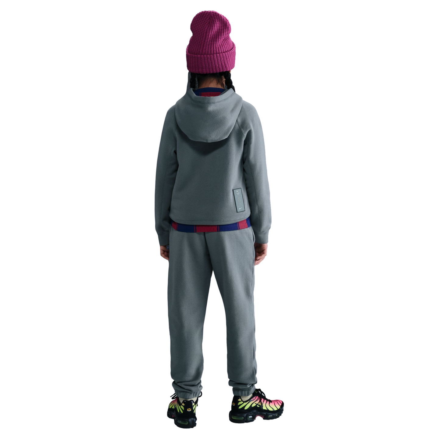 Rear view of a person wearing a grey tracksuit, a magenta beanie, and colorful patterned sneakers against a solid black background.