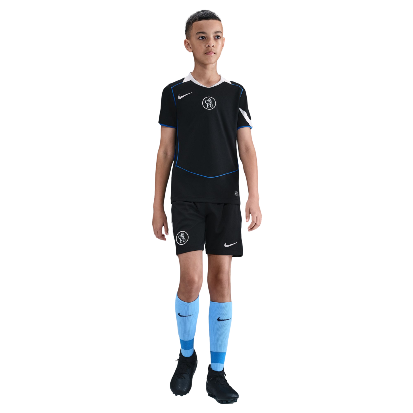 A young boy stands in a black Nike Chelsea FC soccer kit with light blue socks and black cleats, isolated on a black background.