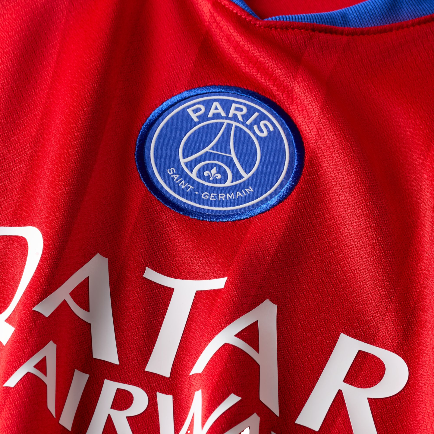 Close-up of a red Paris Saint-Germain football jersey featuring the club's blue circular crest and white sponsor text.