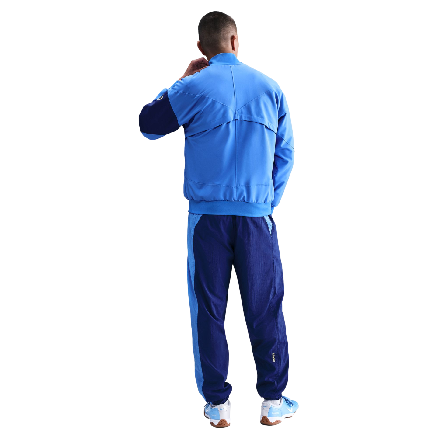 Rear view of a person wearing a two-tone blue Nike tracksuit and matching sneakers against a black background.