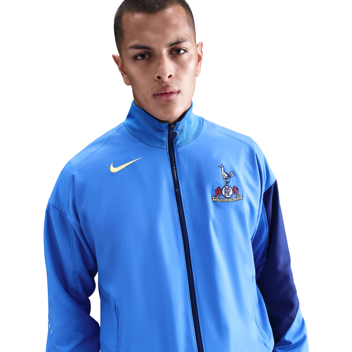 A man wearing a light blue Nike Tottenham Hotspur track jacket against a solid black background.