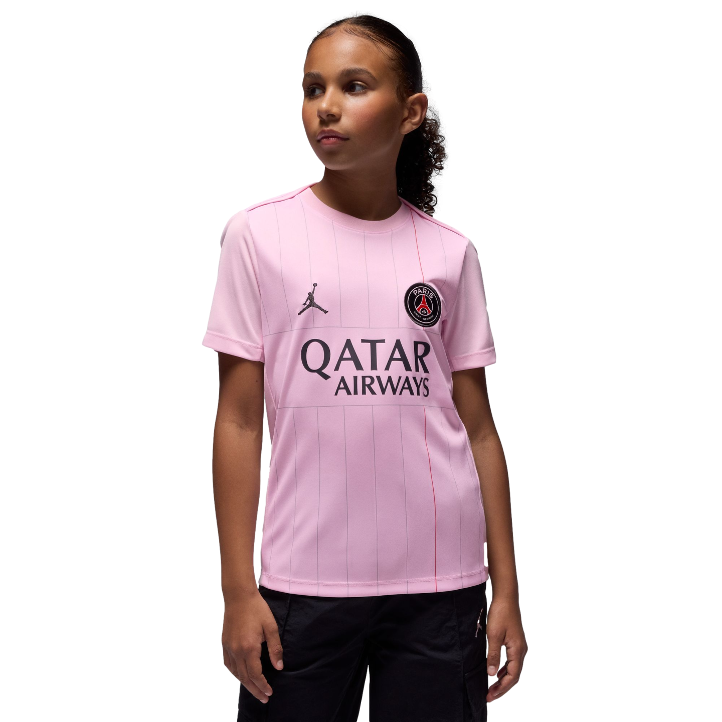 Young girl models a pink PSG jersey with Qatar Airways and Jordan logos against a solid black background.
