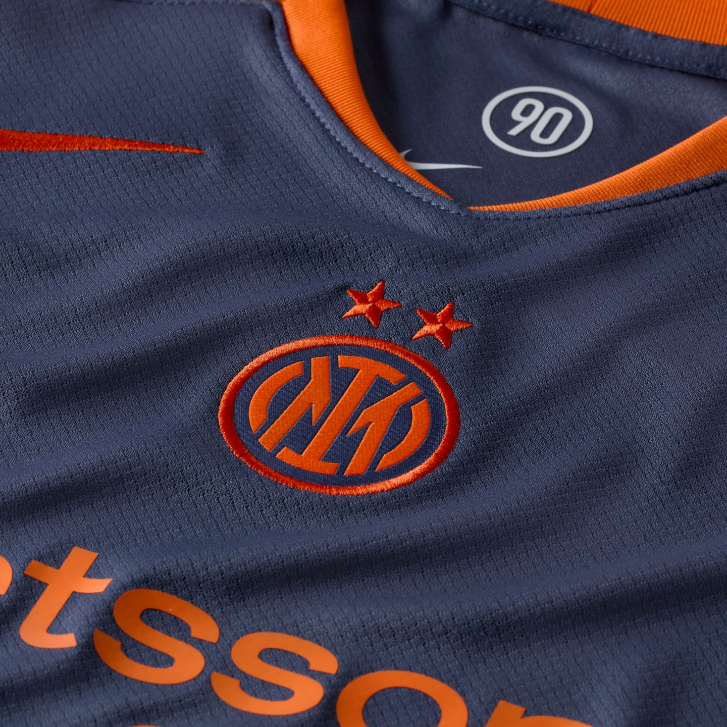 Close-up of a navy blue Inter Milan football kit featuring the embroidered orange club crest with two stars and orange accents on the collar.