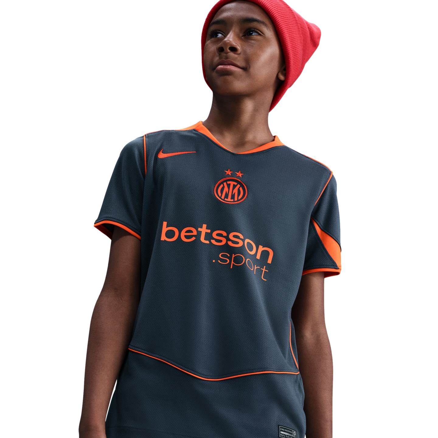 A young person wearing a red beanie and a grey Nike Inter Milan jersey with orange trim and "betsson .sport" branding, looking upward against a black background.
