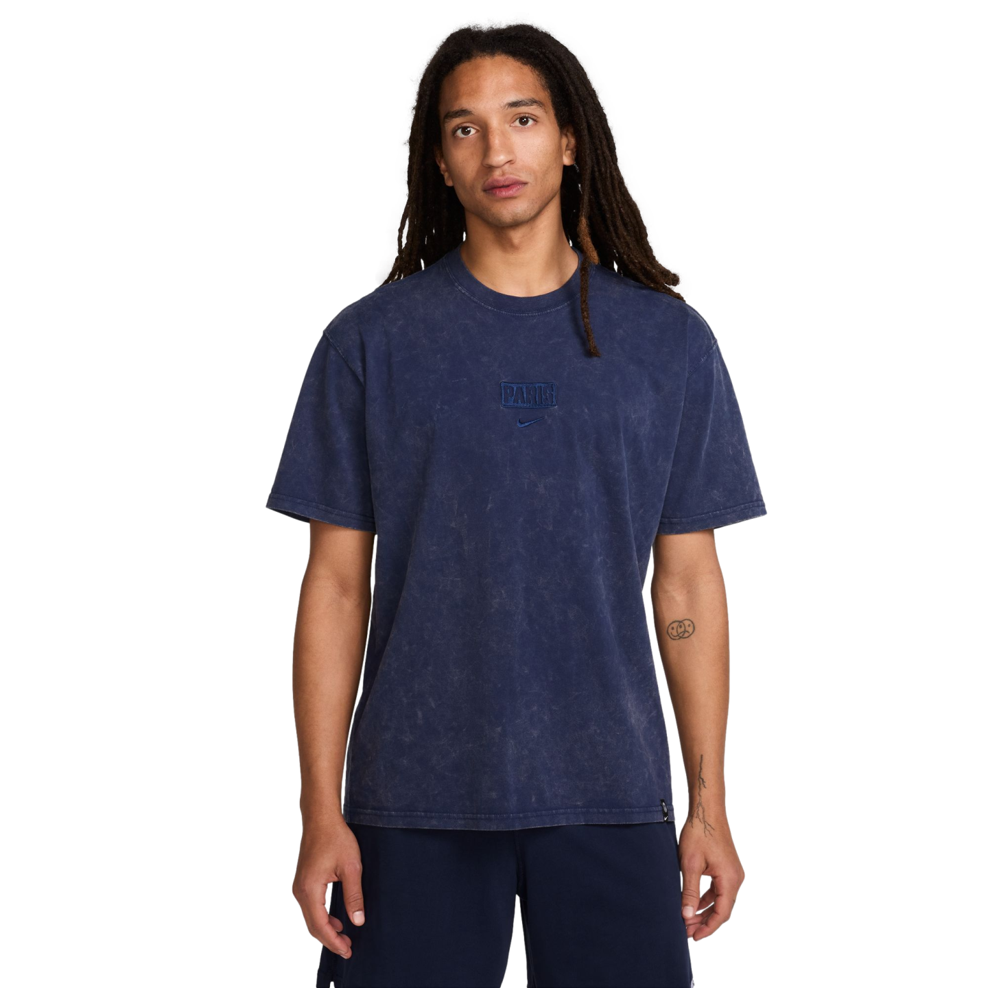 A man with long dreadlocks wears a navy blue acid-wash Nike "PARIS" t-shirt and navy shorts, standing against a white background.