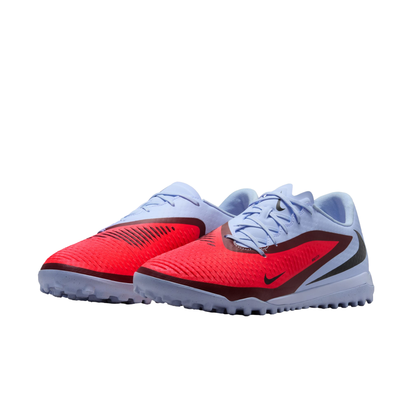 Pair of Nike turf soccer shoes in light blue and bright red, featuring a textured upper and rubber nubbed outsoles, set against a black background.