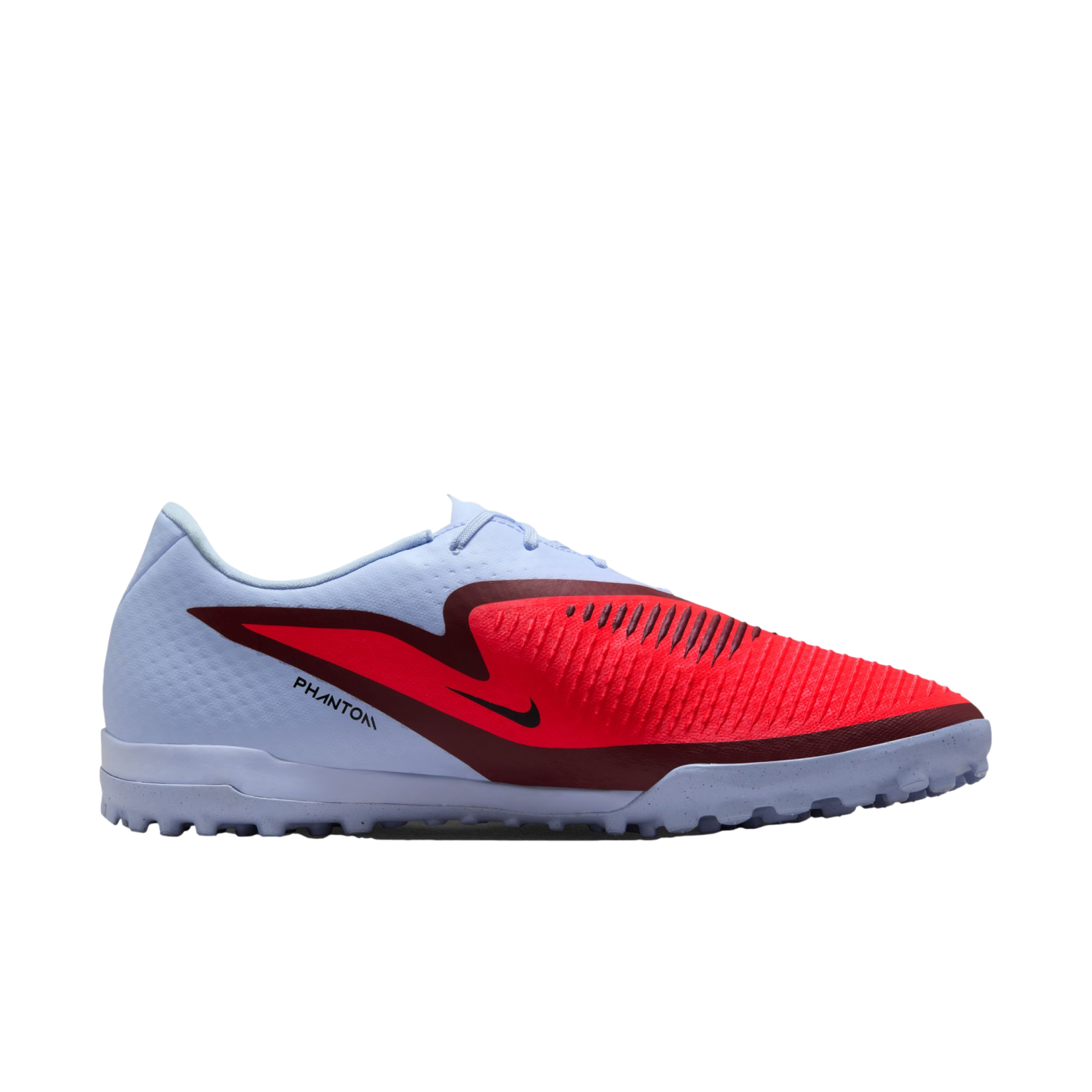A side view of a light blue Nike Phantom turf soccer shoe featuring a bold red and maroon graphic, black swoosh, and textured rubber sole, set against a solid black background.