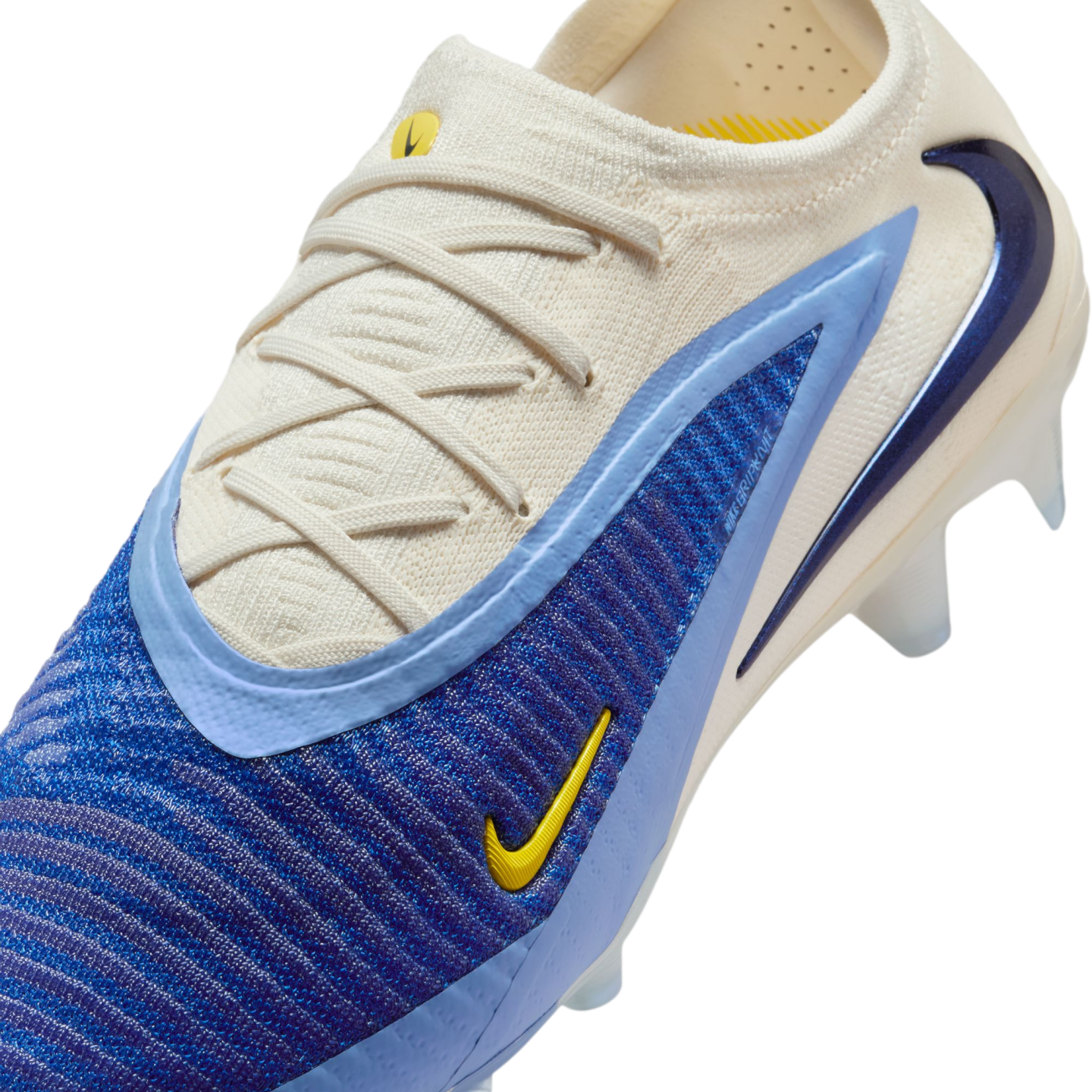 Close-up of a Nike Phantom soccer boot with a cream knit upper, textured blue panels, and a yellow swoosh logo.