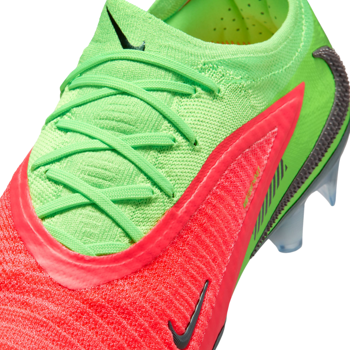A close-up, high-angle view of a vibrant neon green and bright pink Nike soccer cleat against a black background. The shoe features a textured, knitted upper with matching neon green laces and multiple black Nike swoosh logos. Clear, translucent studs are