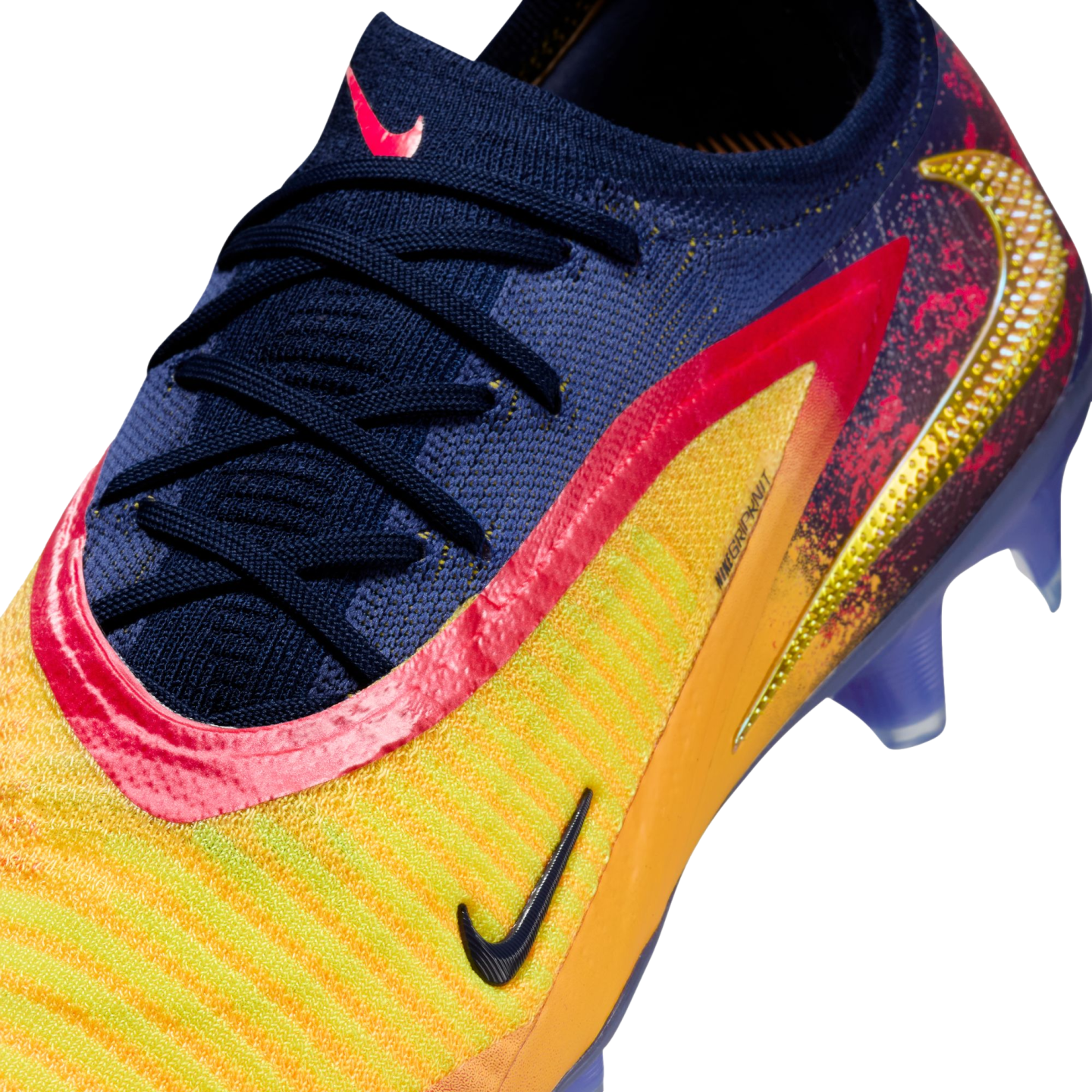 Close-up of a Nike soccer cleat featuring a navy blue knit upper, yellow and orange stripes, pink accents, and a textured gold Swoosh logo.