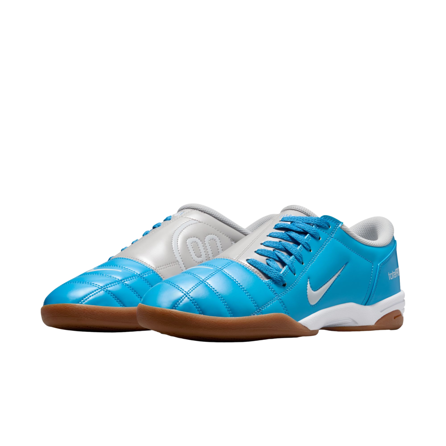 Cyan blue and white Nike Total 90 indoor soccer shoes with gum rubber soles against a black background.