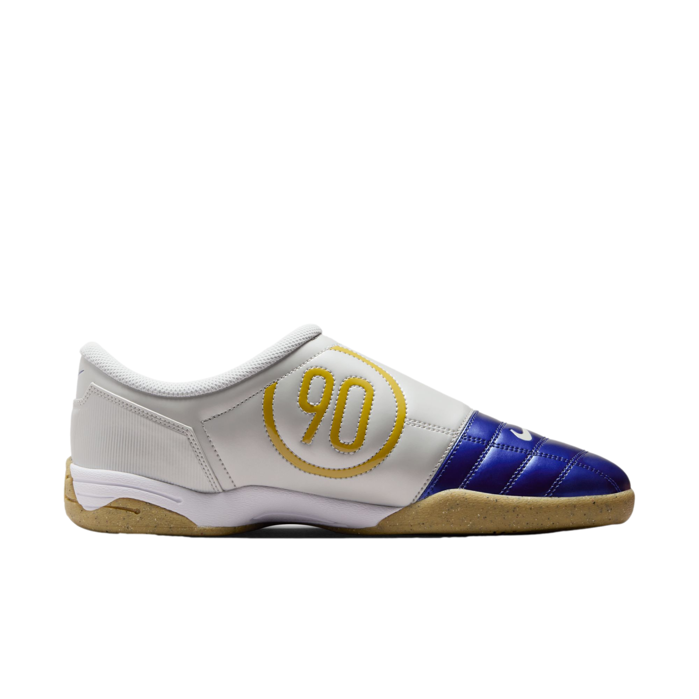 Side view of a white indoor soccer shoe featuring a blue quilted toe box, a yellow "90" logo in a circle on the side, and a gum rubber sole against a black background.
