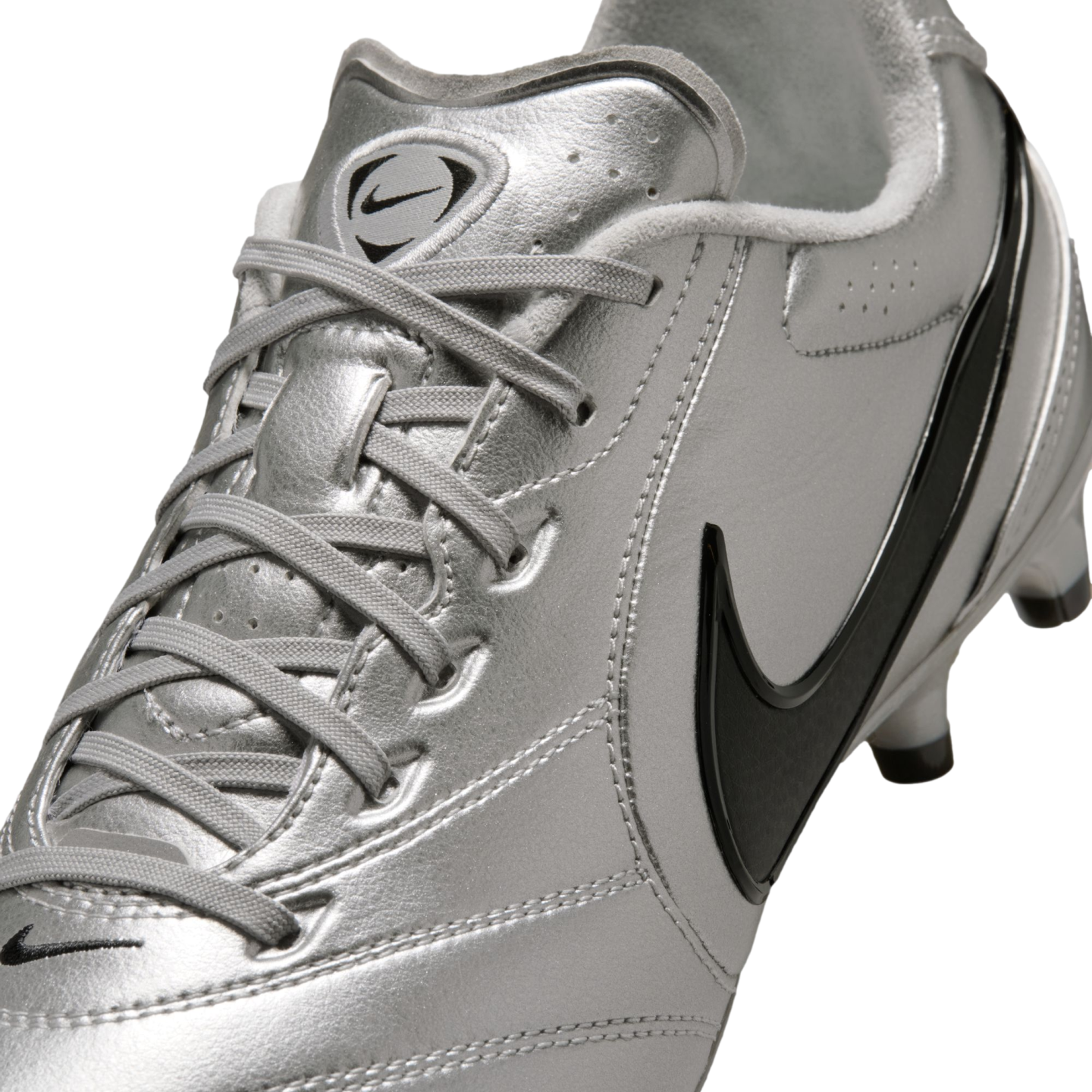 A close-up, angled shot of a metallic silver Nike soccer cleat featuring black swooshes and silver laces against a black background.