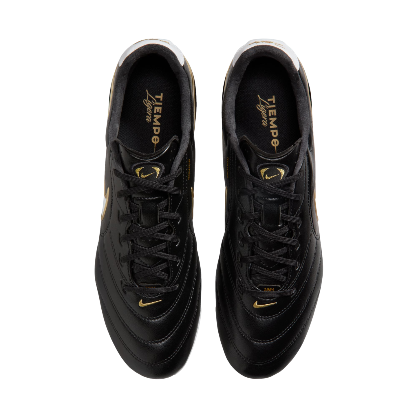 Top-down view of black Nike Tiempo Ligera soccer cleats with gold accents and branding, shown against a solid black background.