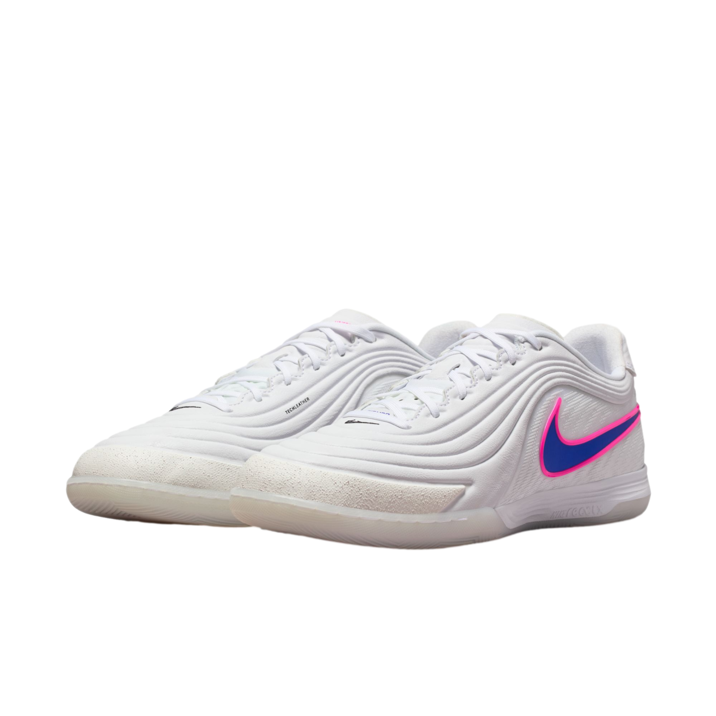 A pair of white Nike indoor soccer shoes with a blue swoosh outlined in pink. The shoes have a textured white upper and translucent outsoles, set against a black background.
