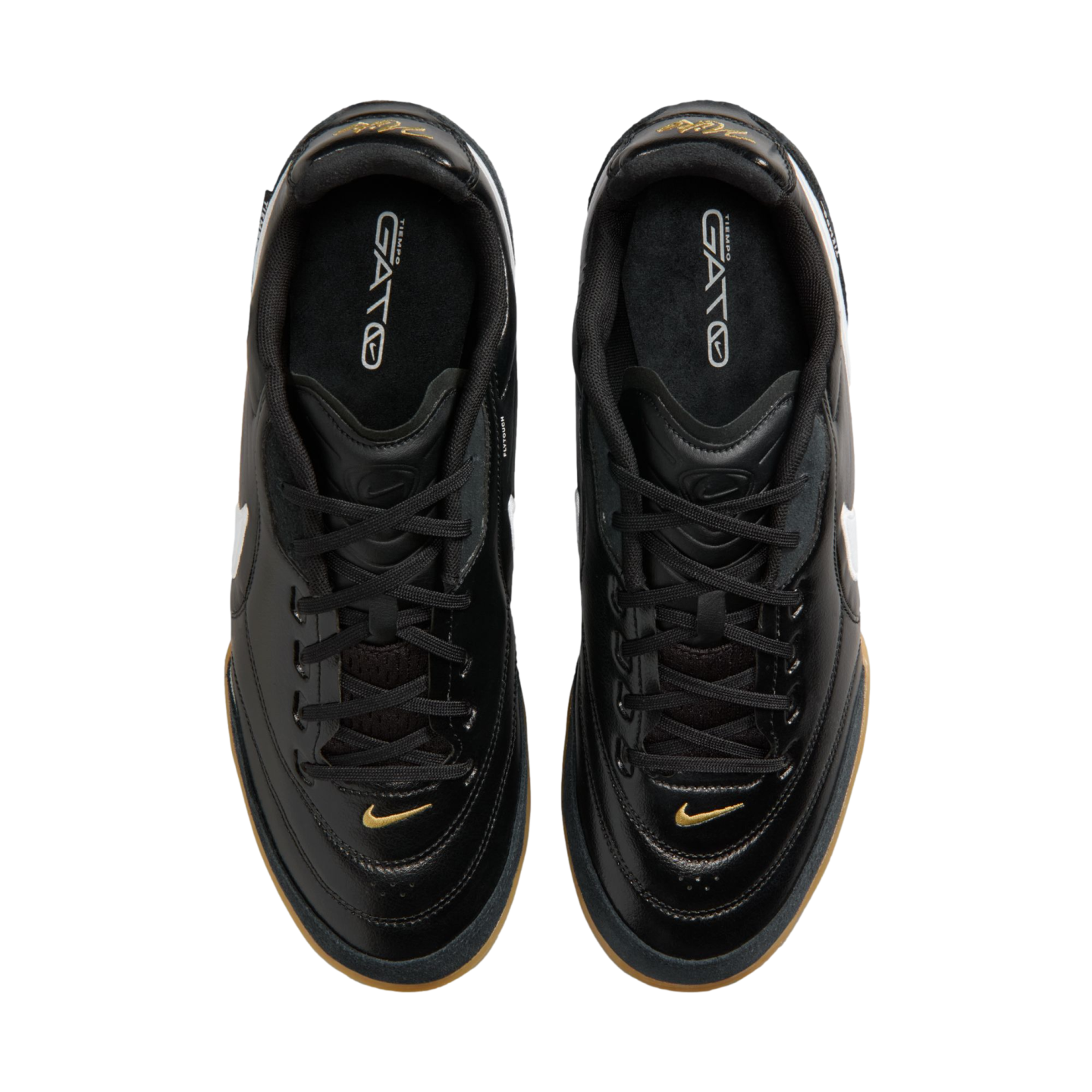 Top-down view of black Nike Tiempo Gato sneakers featuring gold accents and gum rubber outsoles on a solid black background.