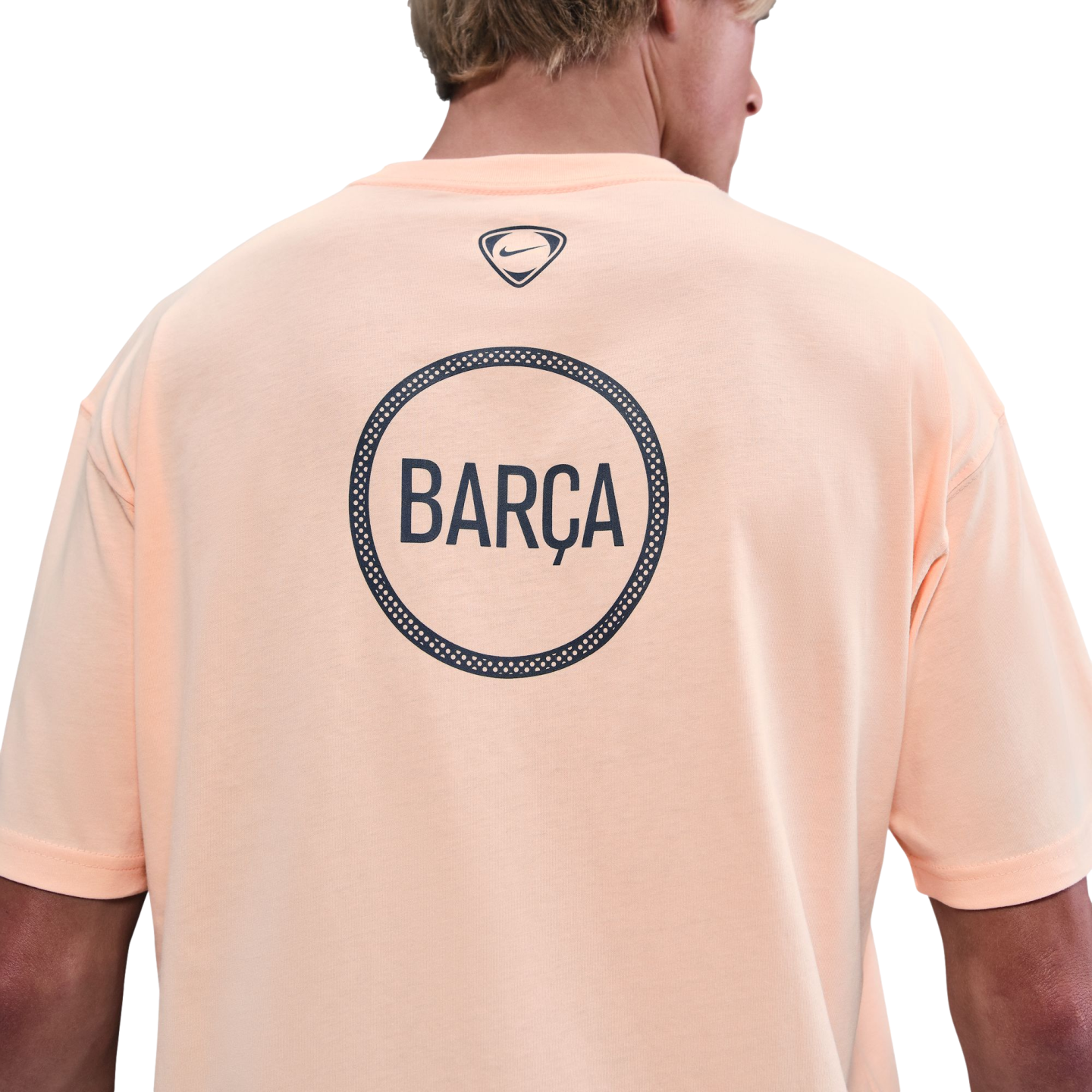 Back view of a person wearing a light orange Nike t-shirt with a large circular "BARÇA" graphic on the back against a black background.