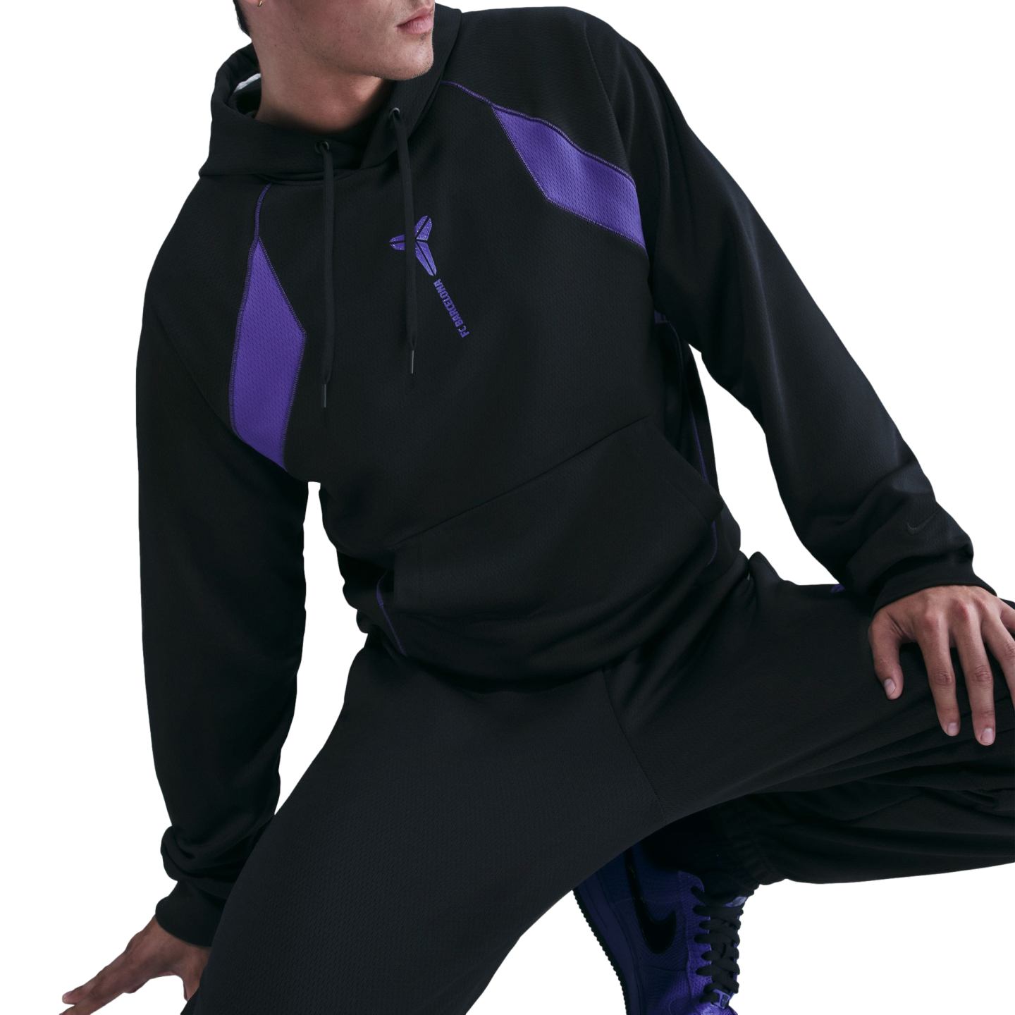 A person posing in a black Kobe Bryant x FC Barcelona hoodie with purple accents and matching black pants.
