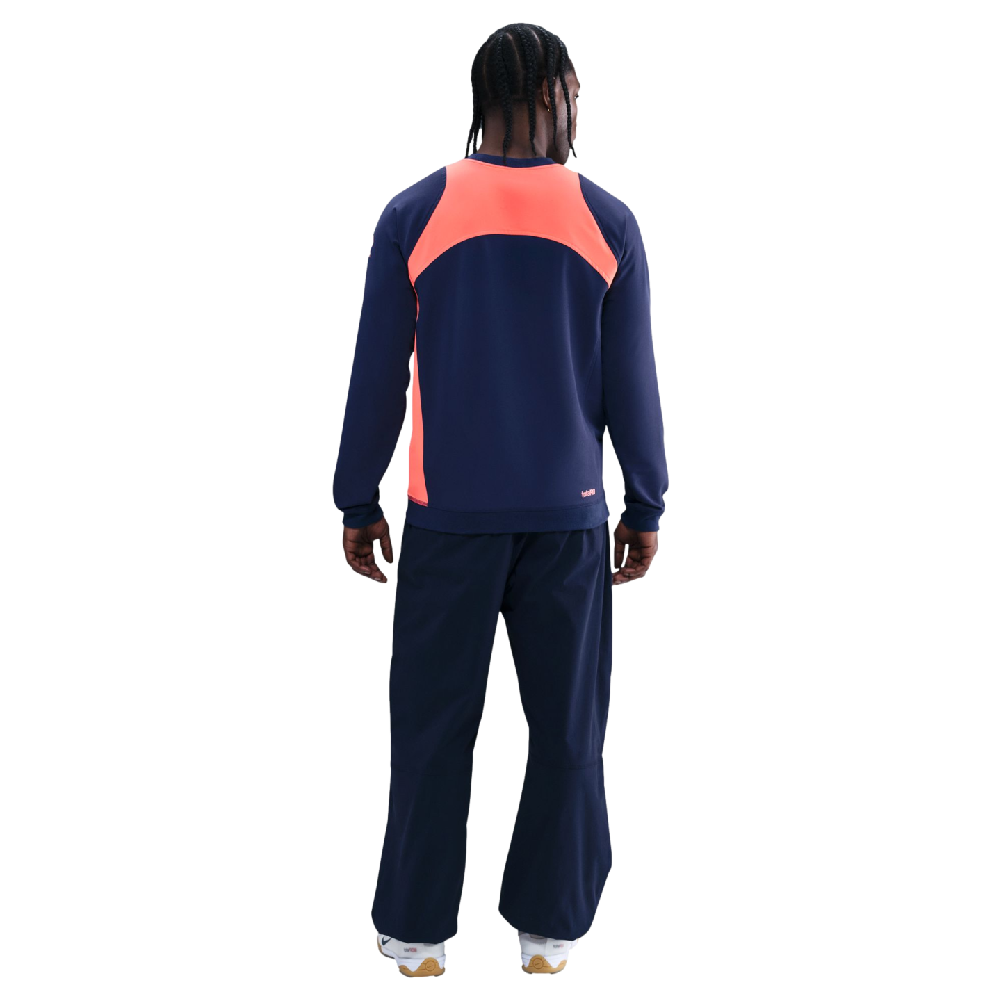 Rear view of a person wearing a navy tracksuit with a bright orange panel across the upper back, against a black background.