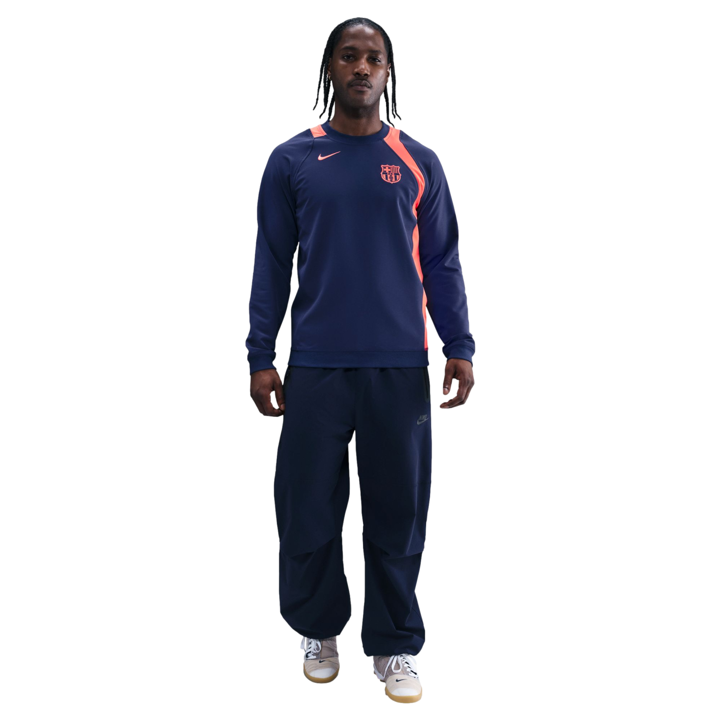 Man in a navy Nike FC Barcelona sweatshirt with orange accents and matching track pants, standing against a black background.
