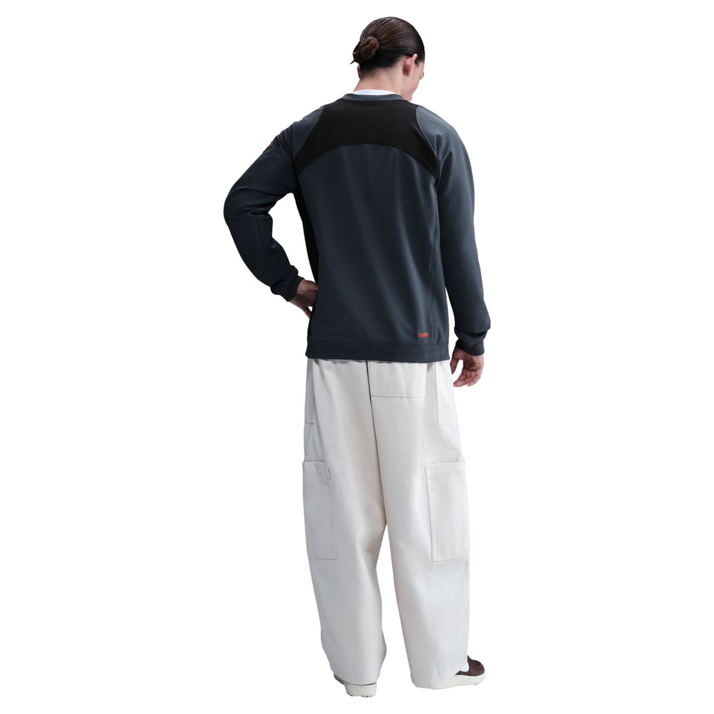 Rear view of a person wearing a dark grey panelled sweatshirt and cream wide-leg cargo pants against a black background.