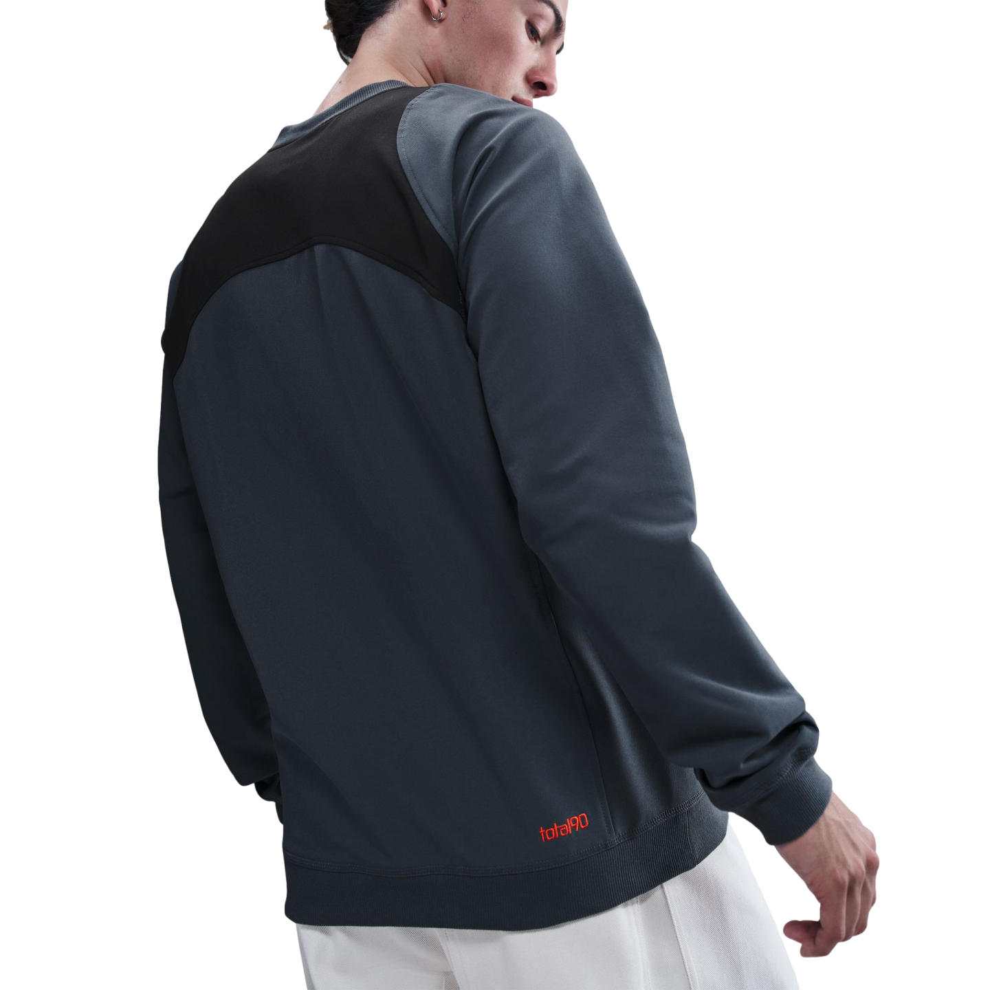 A man seen from behind wearing a grey and black color-blocked sweatshirt with a red logo on the hem and white pants.